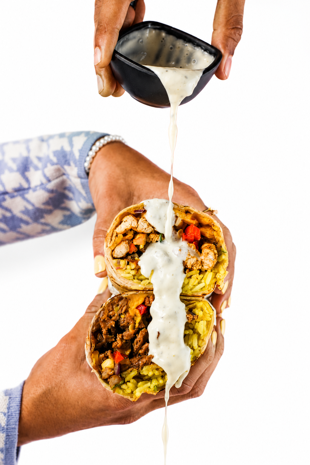 Hands pouring poblano lime crema over a Burrito Rush burrito